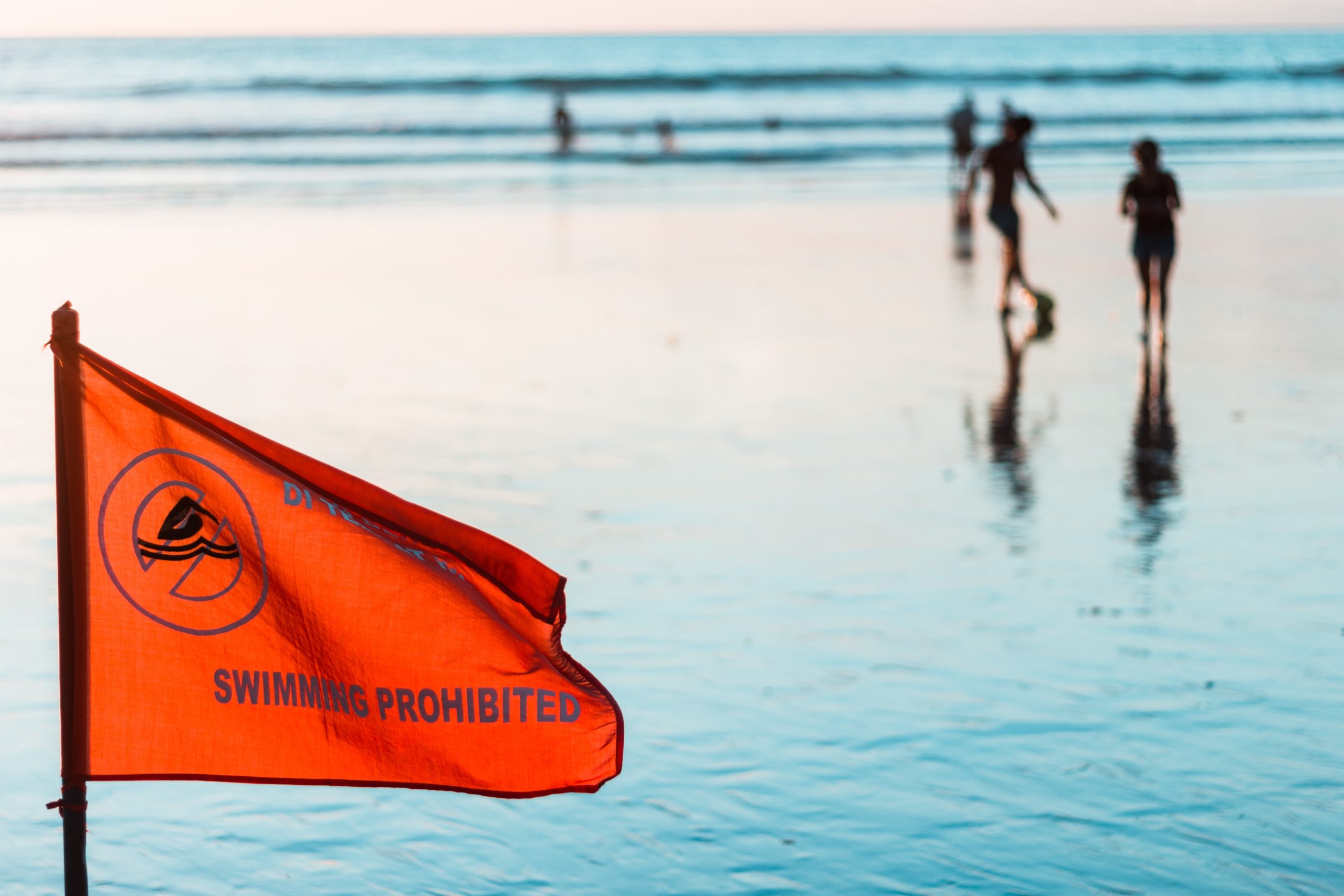 A red flag with the warning "swimming prohibited" flies at the beach. Children play in the water behind it.